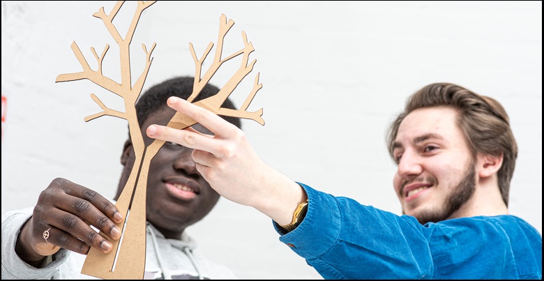 Two Creative Industries students holding up a cut-out of a tree