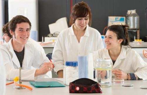 students sitting around a lab bench smiling in white lab coats