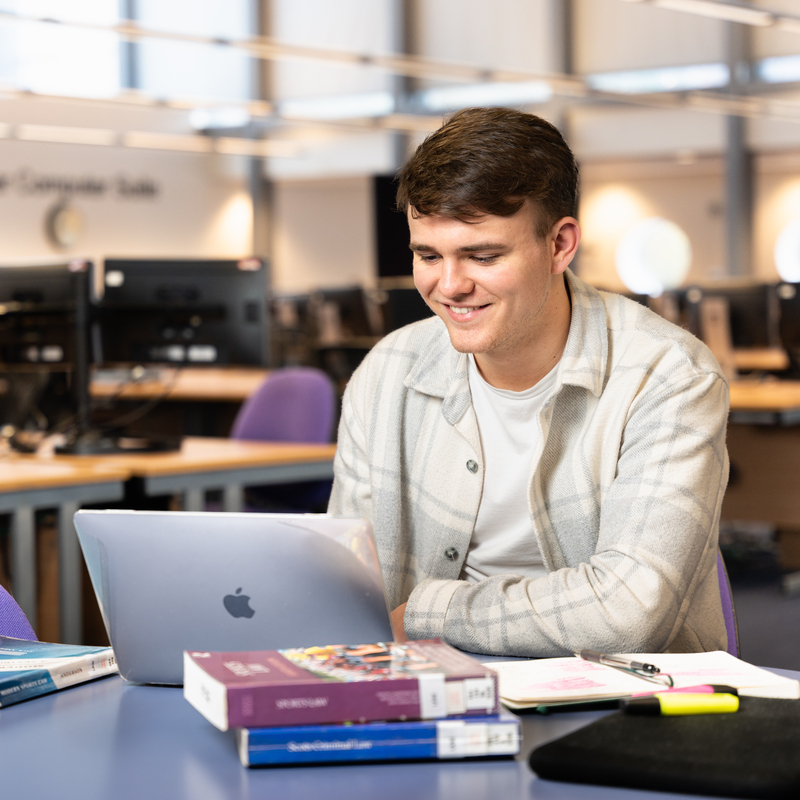Law student Josh Binnington studying in the library at Craiglockhart. Josh is working from a desk with their laptop open and is surrounded by law textbooks. 