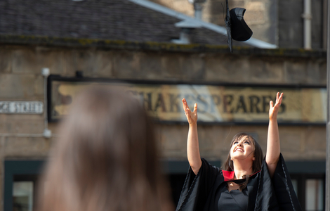 graduating female is throwing her graduation hat in the air outside Usher Hall