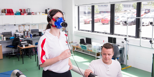 girl running on a treadmill with an oxygen mask on her face, and a sport scientist monitoring her vo2max