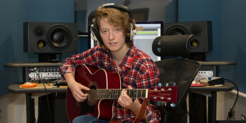 Male Student playing guitar with recording equipment.