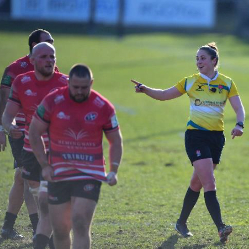Female rugby referee communicating with male rugby players on the pitch
