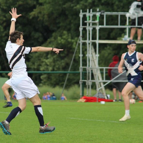 A referee running and pointing on a sports pitch, and a player running towards the referee.