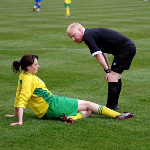 Male sports referee talking to a female player sitting on the ground after a fall on the pitch