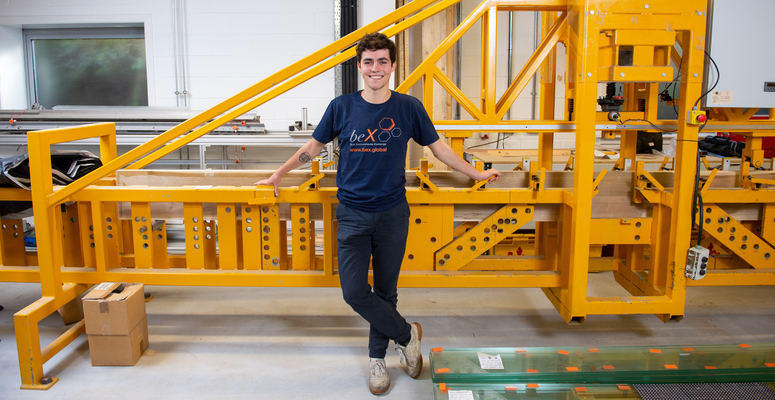 A beX scholar, Victor Henquel, poses next to a wood bending machine