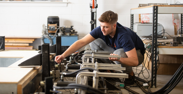 beX scholar, Calum Stuart, crouched down working on a wood machine