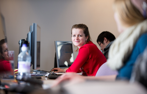 Woman smiling to the camera amongst other Students working with computers