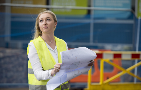 Woman on a building site in high visibility holding engineering drawings