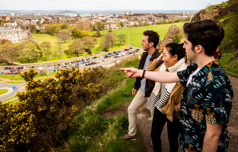 Students climbing Arthur's Seat, looking and pointing down at Edinburgh