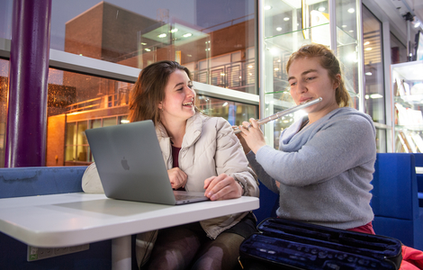 student playing flute whilst her peer watches smiling