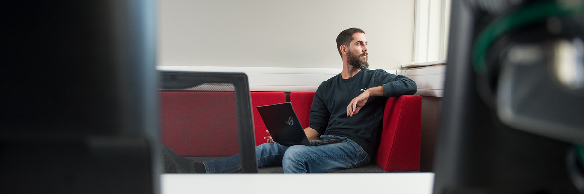 Student sitting with his laptop, looking out the window behind him