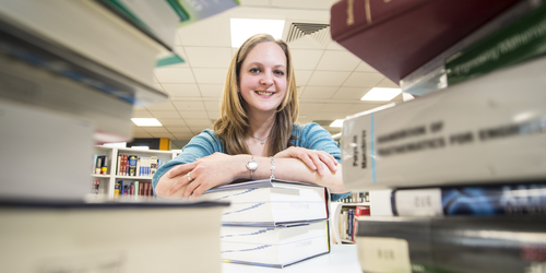 Woman smiling behind stacks of books
