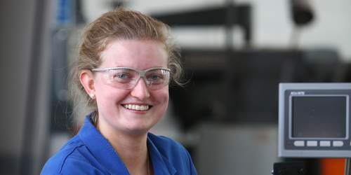 Photo of an engineering student smiling for the camera in engineering lab wearing safety glasses