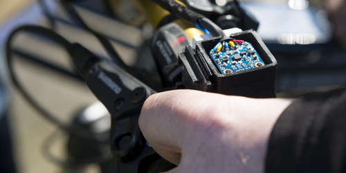 Close up of prototype device mounted on a bicycle, with circuit board visible in a persons hand