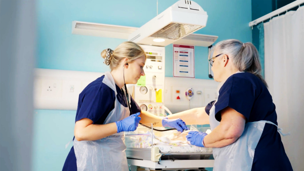 Two healthcare staff provide care to a newborn in a hospital neonatal unit.
