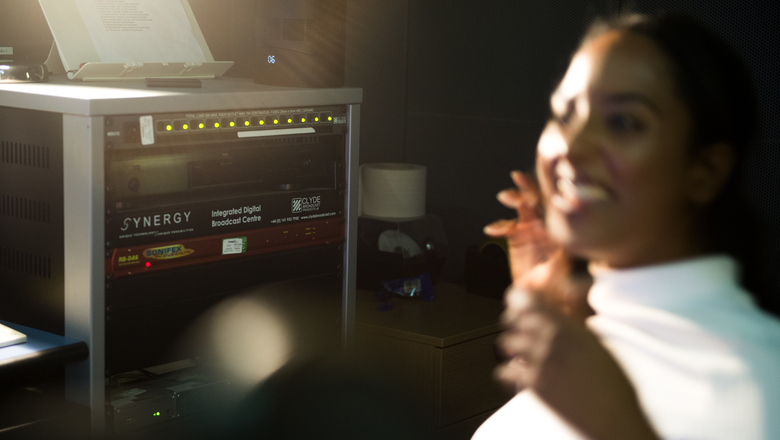 student smiling next to broadcasting equipment