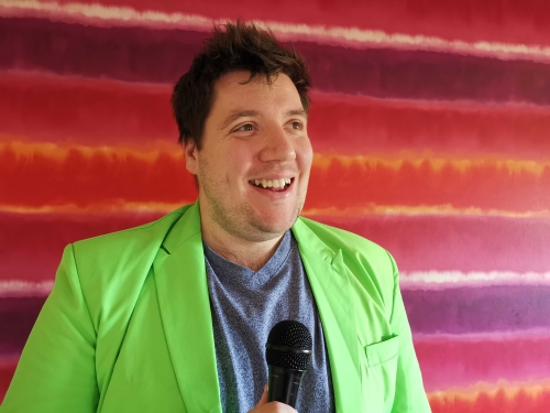 Alumnus Andrew Wildgoose standing in front of a pink and purple patterned canvas