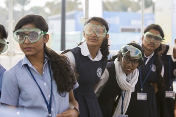 A group of four school children wearing safety goggles, looking to the right of the camera