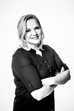 A black and white photo of Mia Ylönen. Smiling at the camera with arms folded