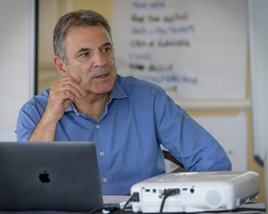 Mike De Luca sitting at a table with a laptop and projector in front of him