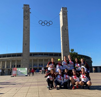 A group of athletes standing in front of two pillars with the Olympic five rings hanging in the air