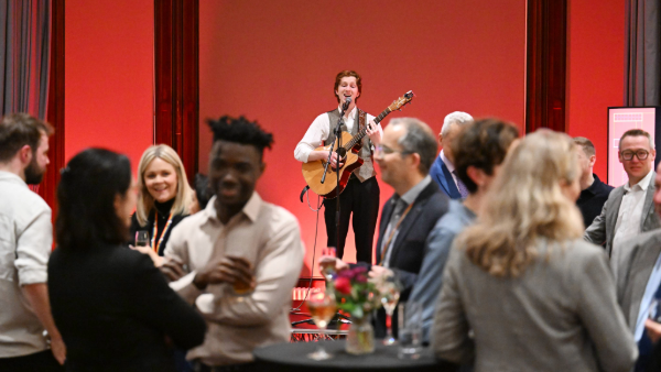 Attendees networking at a previous Alumni Awards Celebration event while musician plays in the background