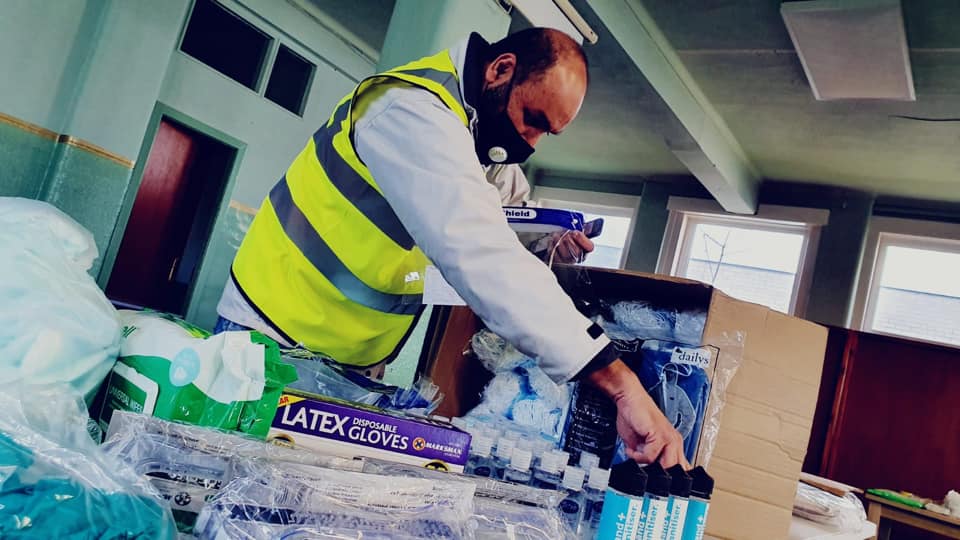 Zahir standing behind a table, sorting through a box of personal protective equipment (PPE)