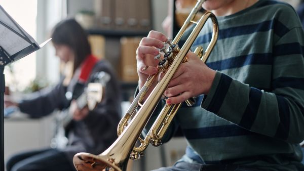 Student playing a trumpet with a guitar player in the background