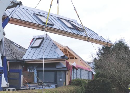 A house roof made from a timber frame being lowered onto the foundation by a crane