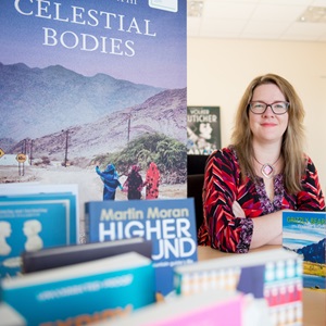 Kay Farrell, sitting at a table, surrounded by books 