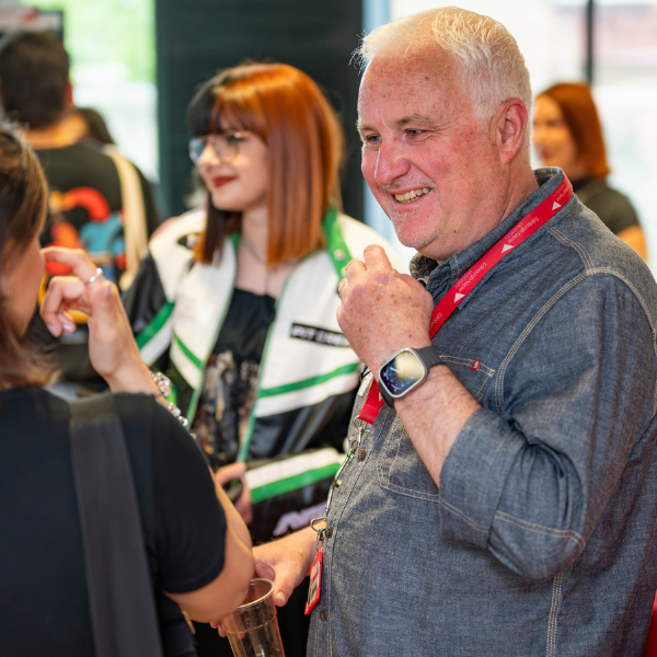 George Shepherd, ENU programme leader, wearing a red lanyard chatting with others at an indoor event while holding a beverage