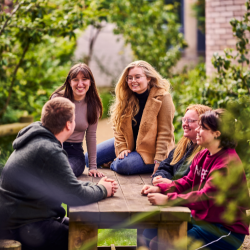 A group of people sitting on a picnic bench surrounded by foliage 