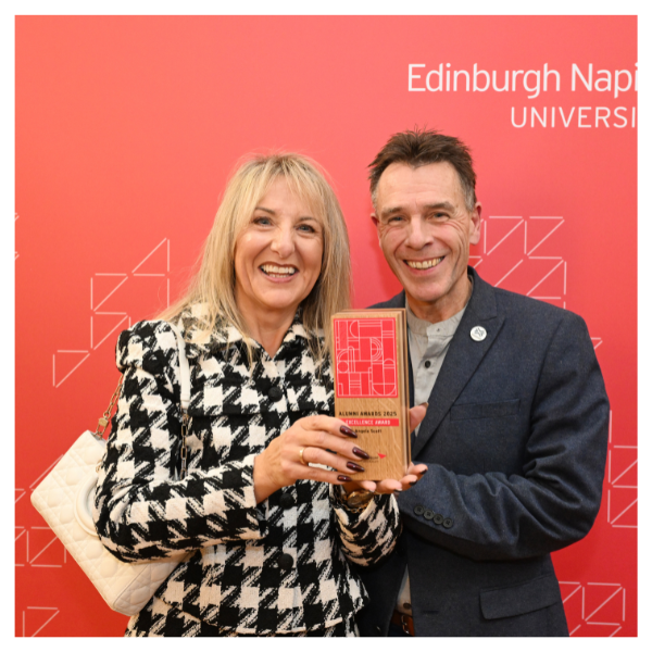Angela Scott holding her Alumni Award trophy, with her husband to her left