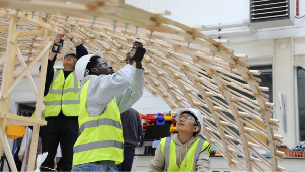 Students assembling a timber structure in a workshop.