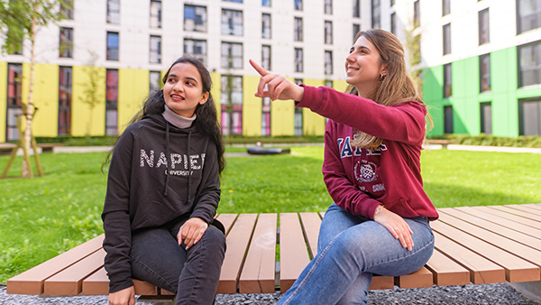 Two students sitting on a bench in grassy courtyard at Bainfield student accommodation