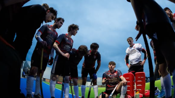 Field hockey team gathered in a huddle during a match break, viewed from the center of the circle.