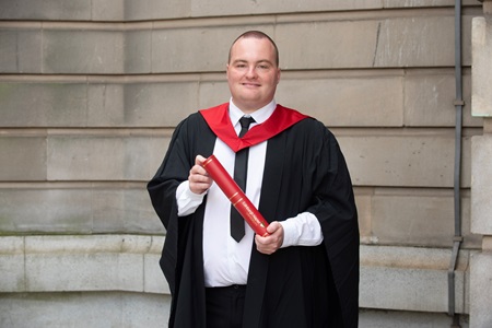 Connor Smith standing with a degree scroll outside the Usher Hall