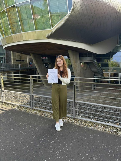 Emma Sullivan holding her dissertation outside Edinburgh Napier University's Craiglockhart campus