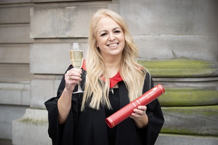 Jilliane McAdam holding her degree and a glass of sparkling wine