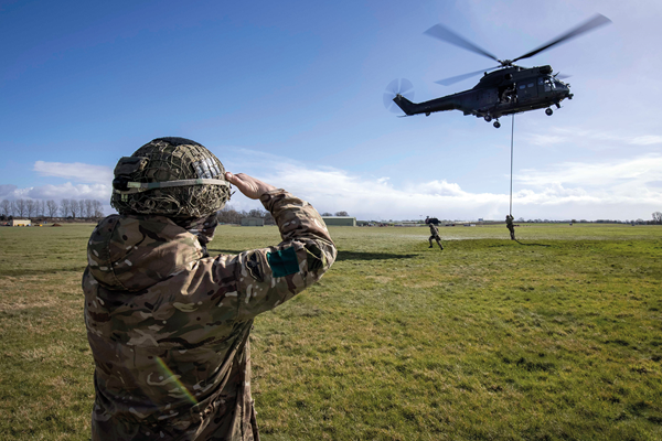A member of the armed forces watches helicopter exercise in field