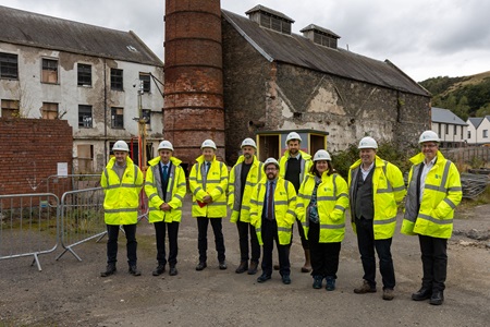 A group of people standing on a building site in hi-vis jackets and hard hats