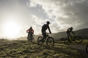 Three bikers cycling past the camera with the sun behind them