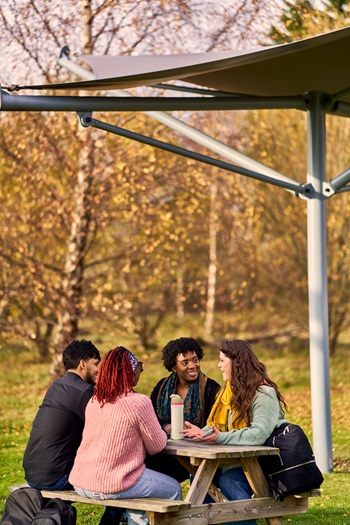 Four students sitting around an outdoor trestle table with foliage in the background