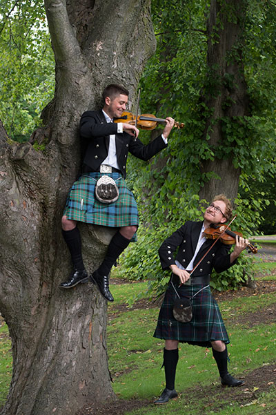 Two Scottish guys wearing kilts and playing the violin outside