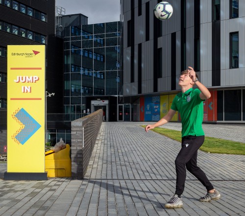 Hibs player Josh O'Connor plays keepie uppie in front of Sighthill signage