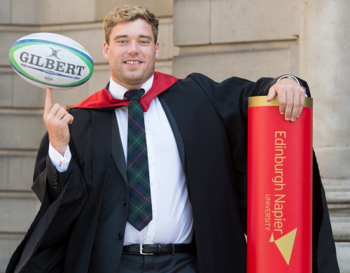 Scotland rugby international Alex Allan posing with a rugby ball and an oversized degree scroll at his graduation