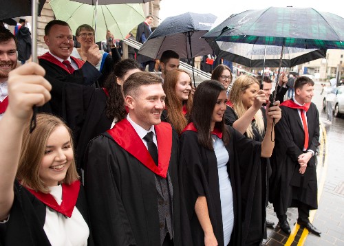The first intake of Graduate Apprentices, with umbrellas, celebrate getting their degrees in the rain outside the Usher Hall  