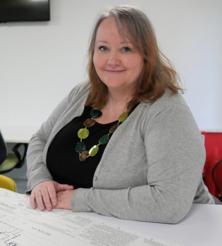 Beverley Gibbs in grey cardigan sitting at her desk