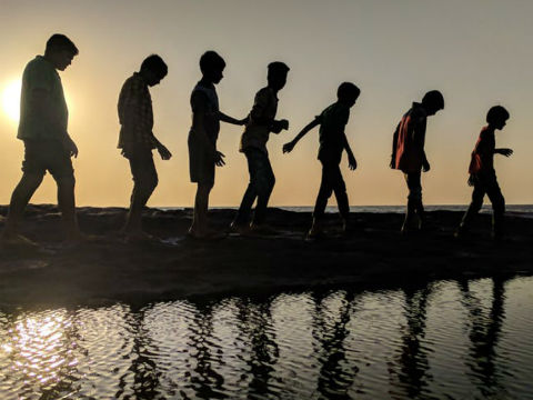 Silhouettes of seven boys walking alongside a river